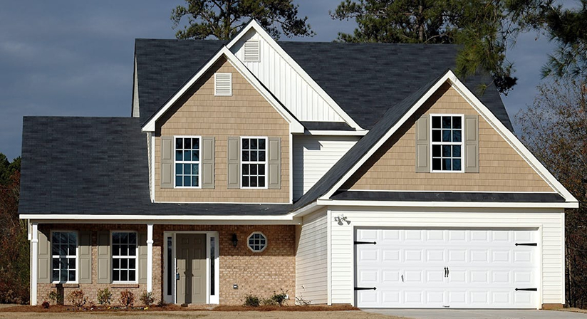 Modern two-story suburban house with gable roof, brown brick exterior, and white garage door on a clear day.