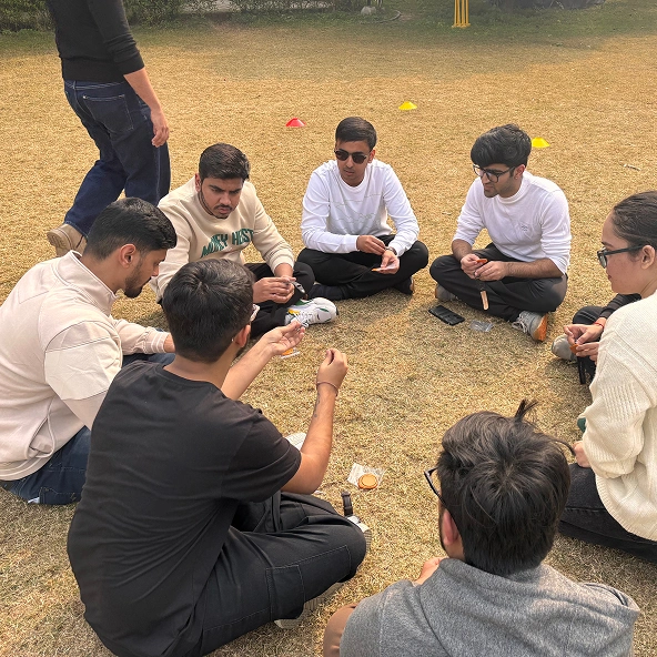 Group of people sitting on grass in a circle, engaging in conversation during an outdoor activity.