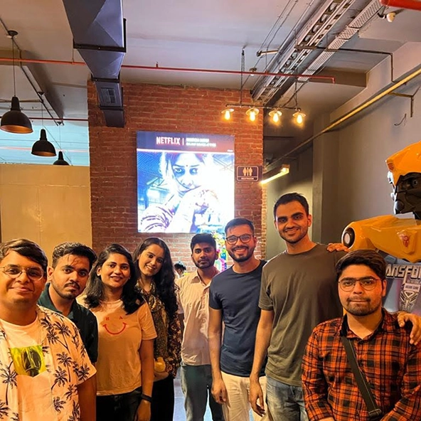 Group of friends at a cafe with a movie poster in the background, standing next to a yellow robot statue.