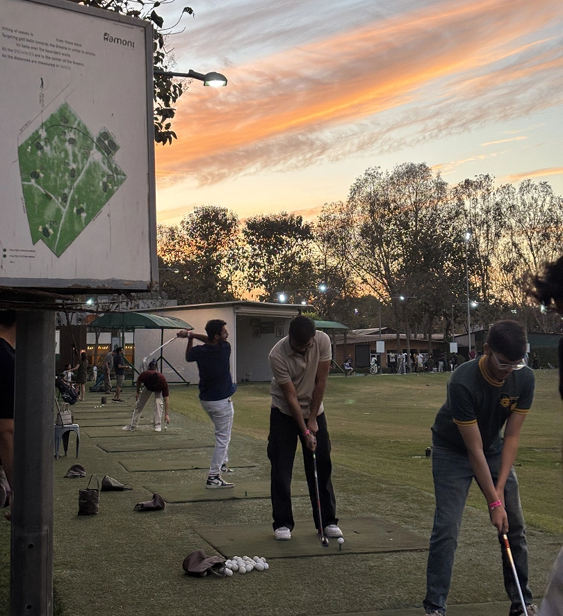 Golfers practice their swings at a driving range during sunset, with a course map visible on the side.