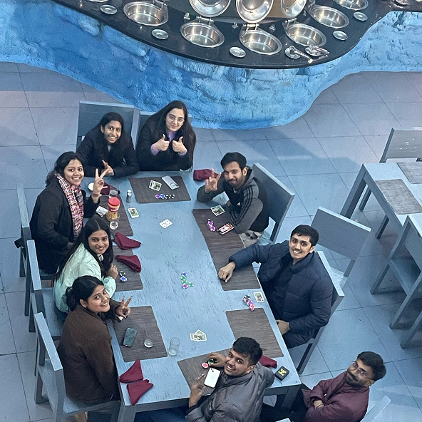 Group of friends enjoying a card game at a restaurant, smiling and showing peace signs and thumbs up.