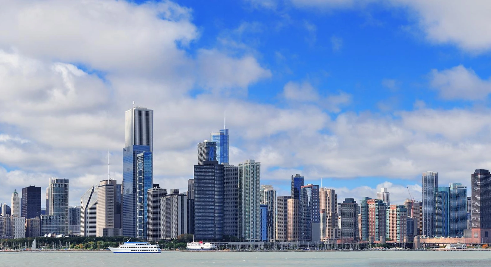 Chicago skyline with skyscrapers against a blue sky, viewed from Lake Michigan, featuring a boat on the water.