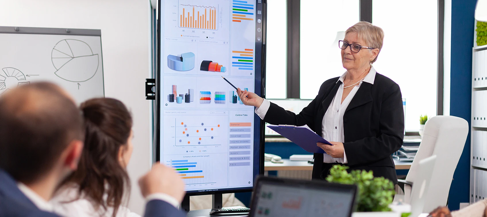 Businesswoman presenting graphs on a monitor to colleagues in a meeting room.