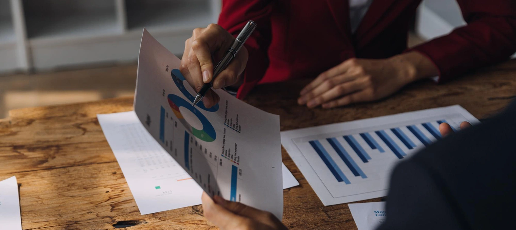 Close-up of hands analyzing financial graphs and charts on wooden desk for business meeting.