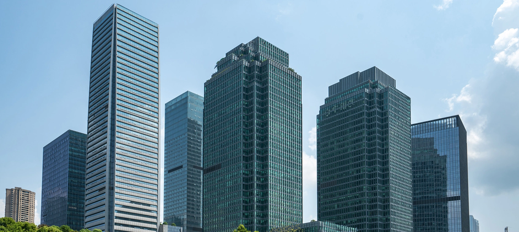 Modern skyscrapers against clear blue sky, showcasing urban architecture with glass facades and greenery at the base.