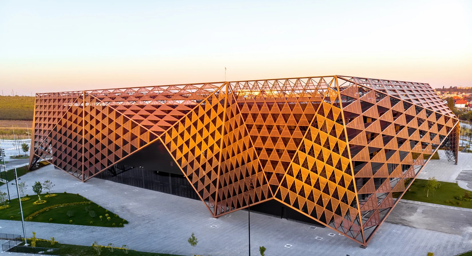 Modern geometric building with triangular patterns illuminated by sunset.