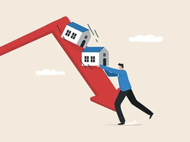 Man stabilizing houses on a plummeting red arrow, symbolizing real estate market decline.